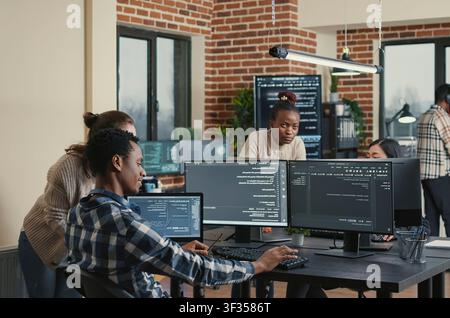 Programmer analyzing compiling code on multiple screens takes off glasses and doing high five hand gesture with colleague developer, software developers celebrating successful coding. Stock Photo