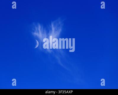 Cloudscape. Concepts - environment. Cirrus clouds and with a waxing crescent moon and deep blue sky. Backgrounds. Copy space. Stock Photo