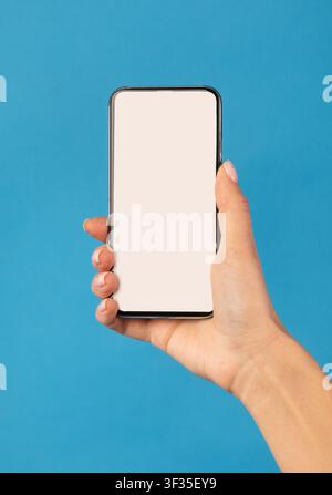 Female Hand Holding Phone With White Screen Over Blue Background Stock Photo