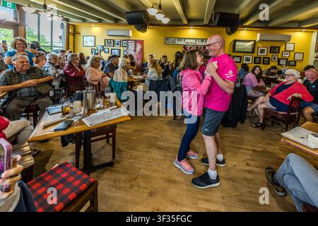 A couple dancing at the KitchenFest festival at the Red Shoe Pub in Mabou, Nova Scotia, Canada. The historic sign reading ‘Beaton’s Clothing – Footwear’ on the wall is a reminder of a former local shop and forms part of the pub’s interior décor. Mabou, Nova Scotia, Canada Stock Photo