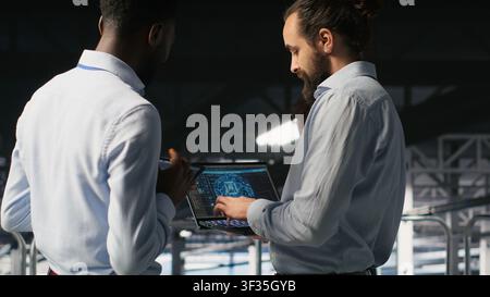 Data center team leader and worker reviewing performance dashboards of AI equipment rigs. Server room supervisor oversees programmer examining machine learning algorithms on screen Stock Photo