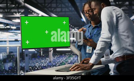 Server hub colleagues doing brainstorming, using chroma key device to review diagnostics. Employees doing maintenance tasks in data center, looking at green screen display Stock Photo