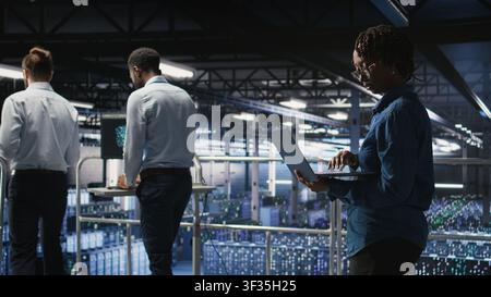 Data center teamworking colleagues running diagnostics on equipment to identify errors, doing brainstorming. Engineering team preventing rigs failure to minimize downtime, Stock Photo