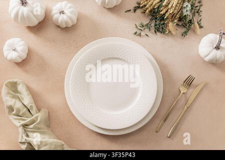 Elegant autumn table setting with white ceramic plates, mini pumpkins and dried flowers on beige background. Thanksgiving concept. Top view, flat lay, Stock Photo