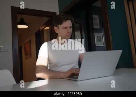 Focused young man works on a laptop while concentrating on a task in a modern apartment in Prague, Czech Republic. Stock Photo