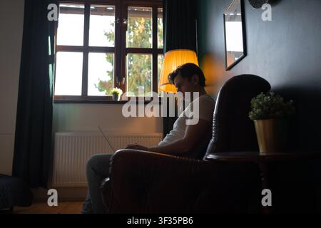 Young man works remotely on a laptop while sitting in a leather armchair in an apartment in Prague, Czech Republic. Stock Photo
