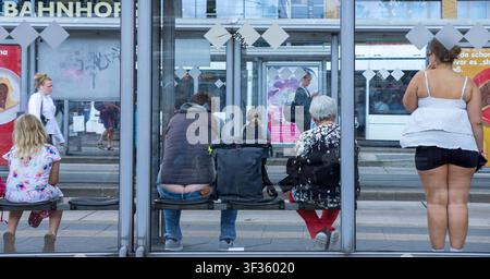 People waiting at a public bus stop in a German city. Germans are waiting for the bus. Warten auf den Bus. Passengers, commuters, passersby. Stock Photo