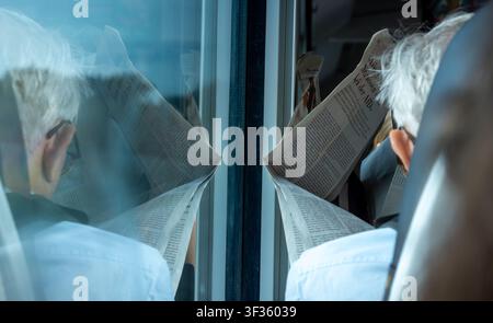 Senior passenger reading a printed newspaper during a train journey in Germany. An older passenger is reading a newspaper. Zeitung lesen. Stock Photo