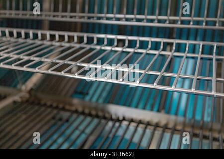 Close-up of empty metal wire shelves in a commercial refrigerator with blue lighting background Stock Photo