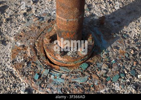 Extreme close-up of a heavily corroded industrial pipe flange and vertical pipe section, displaying thick layers of peeling turquoise paint and deep o Stock Photo