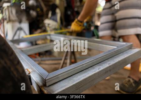 A metal square frame on workbench with hands measuring tape and workshop tools creating focused industrious scene of fabrication and construction Stock Photo