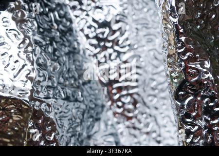A silver textured reflective foil with crinkled surface and abstract highlights creating metallic patterns and soft bokeh reflections, conveying cool Stock Photo
