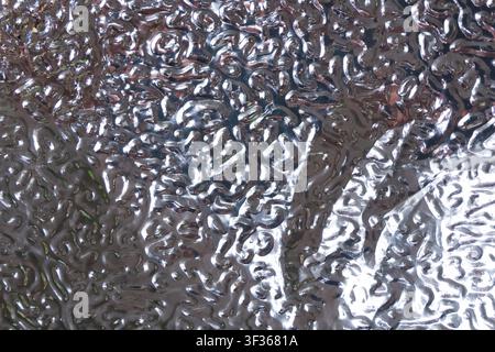 A textured metallic surface with organic ripple pattern, reflective silver finish, abstract closeup showing light and shadow, modern industrial detail Stock Photo