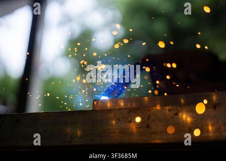 A welding spark and blue arc with metalwork closeup, dynamic orange sparks flying and blurred green background conveying energy and focus Stock Photo