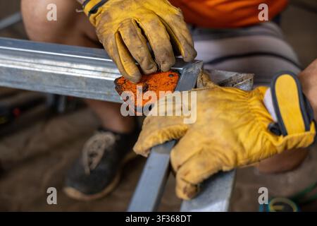 A worker wearing leather glove holds metal frame and welding magnet in workshop showing hands, tool, metalwork and focused craft Stock Photo
