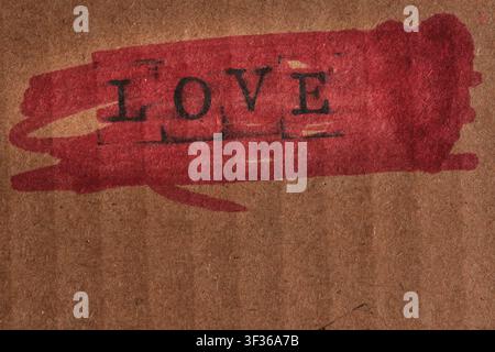 Word LOVE stamped over bright red painted brush stroke on textured brown cardboard paper Stock Photo