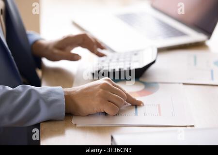 Closeup bookkeeper analyzing charts and using calculator to perform calculations Stock Photo