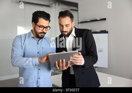 Two multiethnic male colleagues working on project using digital tablet Stock Photo