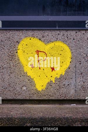 Bright yellow heart stencil with a spray painted red letter P on a rough concrete wall texture. Stock Photo
