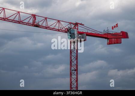 Red Potain tower crane featuring a flying Canadian flag against a cloudy overcast sky in Vancouver, British Columbia. Stock Photo