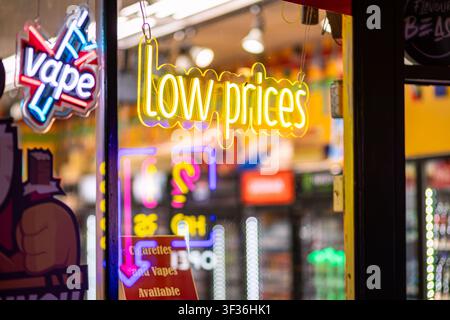 Illuminated LED neon signs advertising low prices and vapes in a convenience store window on Commercial Drive in Vancouver, British Columbia. Stock Photo