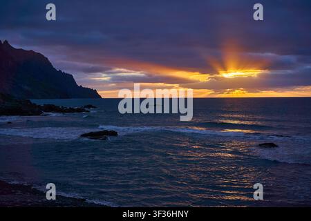 Golden sun rays bursting through clouds over the Atlantic with the silhouetted Anaga coast at sunset Stock Photo