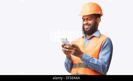 African Builder Worker Using Smartphone On White Studio Background, Panorama Stock Photo
