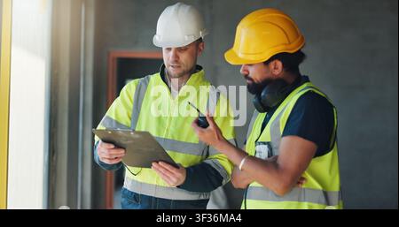 Construction, radio and men with clipboard on site for building progress, compliance or feedback. Team, architect or project manager with checklist Stock Photo