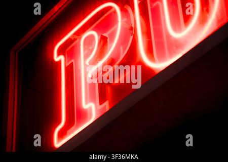 Close up detail of a glowing red neon letter P from a pub sign illuminated against a dark background at night. Stock Photo