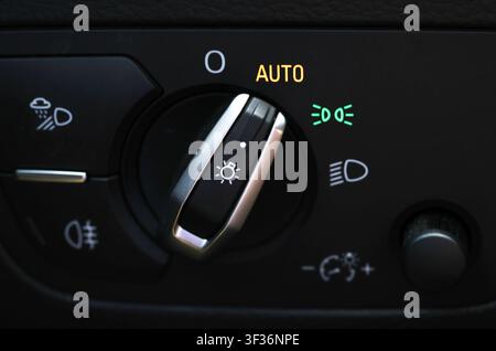 Close up view of car light control knob, showing switch in auto mode with dipped beam indicator illuminated. Dashboard dimmer dial visible. Concept of Stock Photo