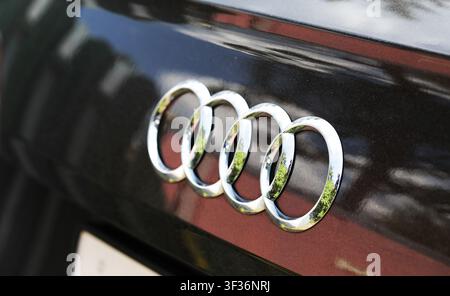 Close-up of chrome logo, four rings symbolizing unity and strength, against dark painted surface of vehicle. Subtle dust particles visible on car pain Stock Photo