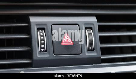 Detailed view of car interior, focusing on hazard warning light button with red triangle symbol. Air conditioning vents flank button with textured rot Stock Photo