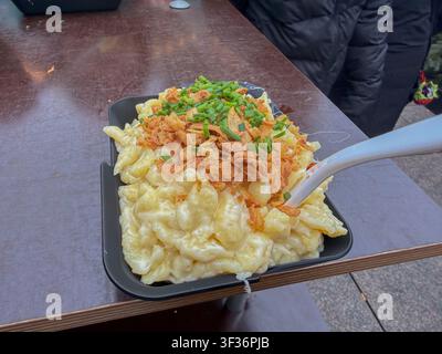 ULM, GERMANY - DECEMBER 13, 2025: Portion of traditional Swabian Kaesspaetzle with fried onions and chives served at the Ulm Christmas Market. Stock Photo