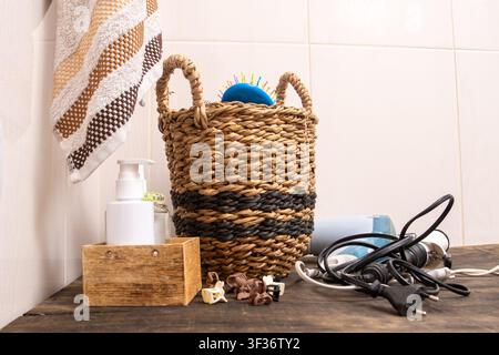 Bathroom Counter Organization with Woven Basket. Hairdryer, towel, curling iron and combs in bathroom at home. Hairpins and hair care and styling items. Stock Photo