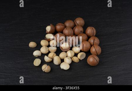 Macadamia nuts scattered. Natural raw peeled macadamia seeds and shells, the hardest and most expensive nuts in the world on black background Stock Photo