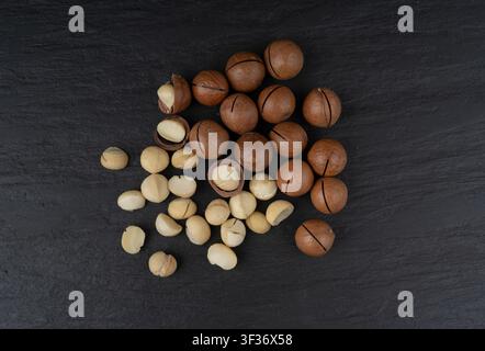 Macadamia nuts scattered. Natural raw peeled macadamia seeds and shells, the hardest and most expensive nuts in the world on black background top view Stock Photo