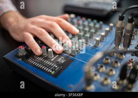 Hands adjusting audio mixer controls on blue soundboard Stock Photo