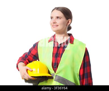 Smiling female construction worker in a safety vest holding a yellow hard hat, looking up with a thoughtful expression Stock Photo