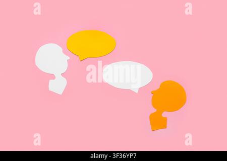 Paper human heads with blank speech bubbles on pink background Stock Photo