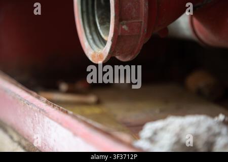 rusty metal pipe attached to red structure in deteriorating industrial environment close-up perspective. industrial maintenance and construction site Stock Photo