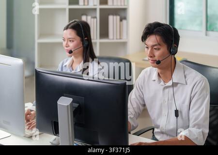 Asian call center agents with headsets working at computers in modern office Stock Photo