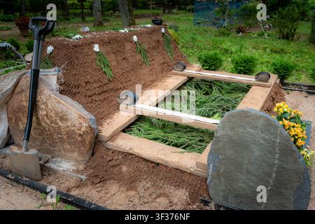 Prepared grave with lowering straps and shovel in cemetery Stock Photo