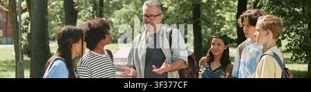 Header of Middle Aged Male Teacher Guiding Diverse Teen Students Outdoors Stock Photo