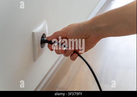 Hand inserting or removing black plug and cable from white wall socket, everyday life and home interior Stock Photo