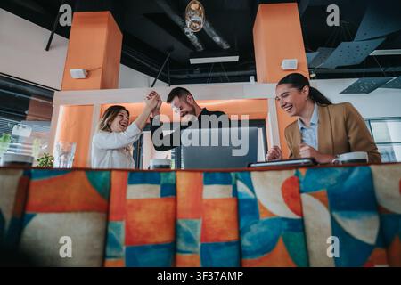 Colleagues celebrating a successful remote work project in a modern office with laptop and smiles Stock Photo