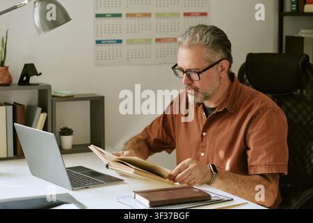 Middle Aged Male Teacher Working by Laptop in School Classroom Stock Photo