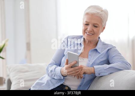 Modern Technologies For Seniors. Smiling Elderly Lady Using Smartphone At Home Stock Photo