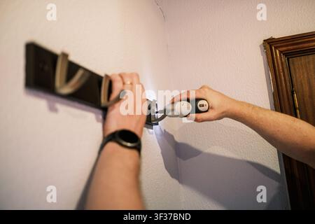 Person is installing a coat rack on a wall using a cordless electric screwdriver Stock Photo