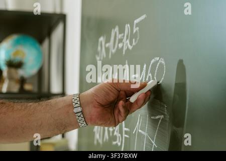 Male Teacher Writing Math Lesson on Chalkboard in Classroom Stock Photo