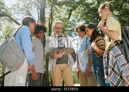Diverse Teen Students Learning with Teacher Using Tablet Outdoors Stock Photo